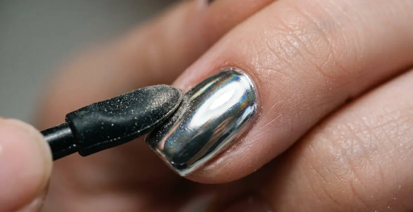 Extreme macro detail of chrome nail powder application showing mirror-like reflective finish and precise sealing technique