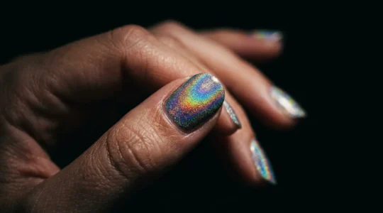 Close-up of holographic nail polish displaying rainbow diffraction effect under dramatic lighting