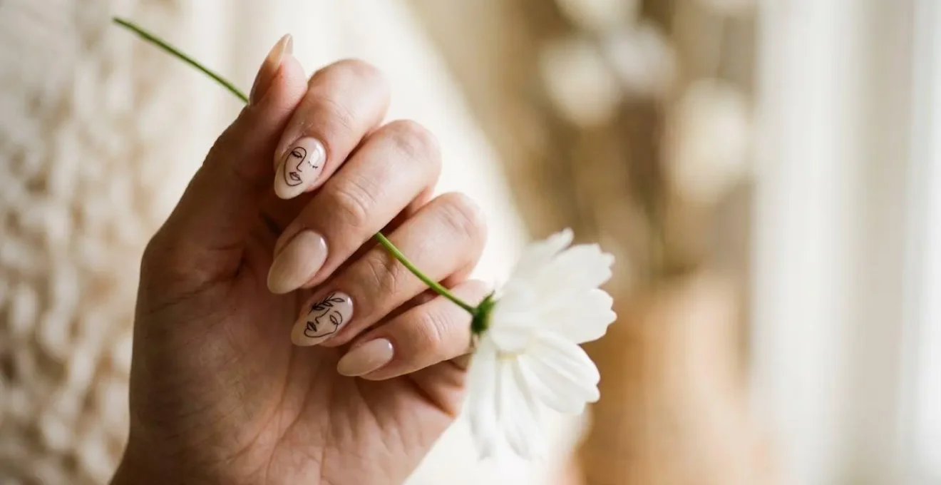Close-up of relaxed hand naturally positioned holding a delicate flower stem showcasing nail art in soft natural light