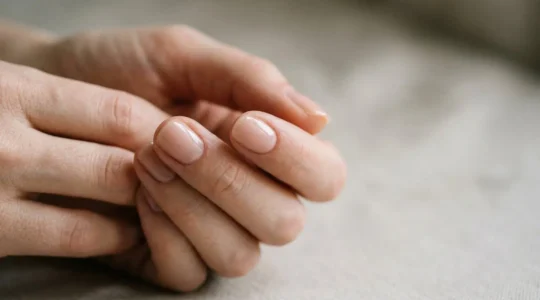 Close-up of hands with perfectly matched nude nail polish showcasing natural skin undertones in soft natural lighting